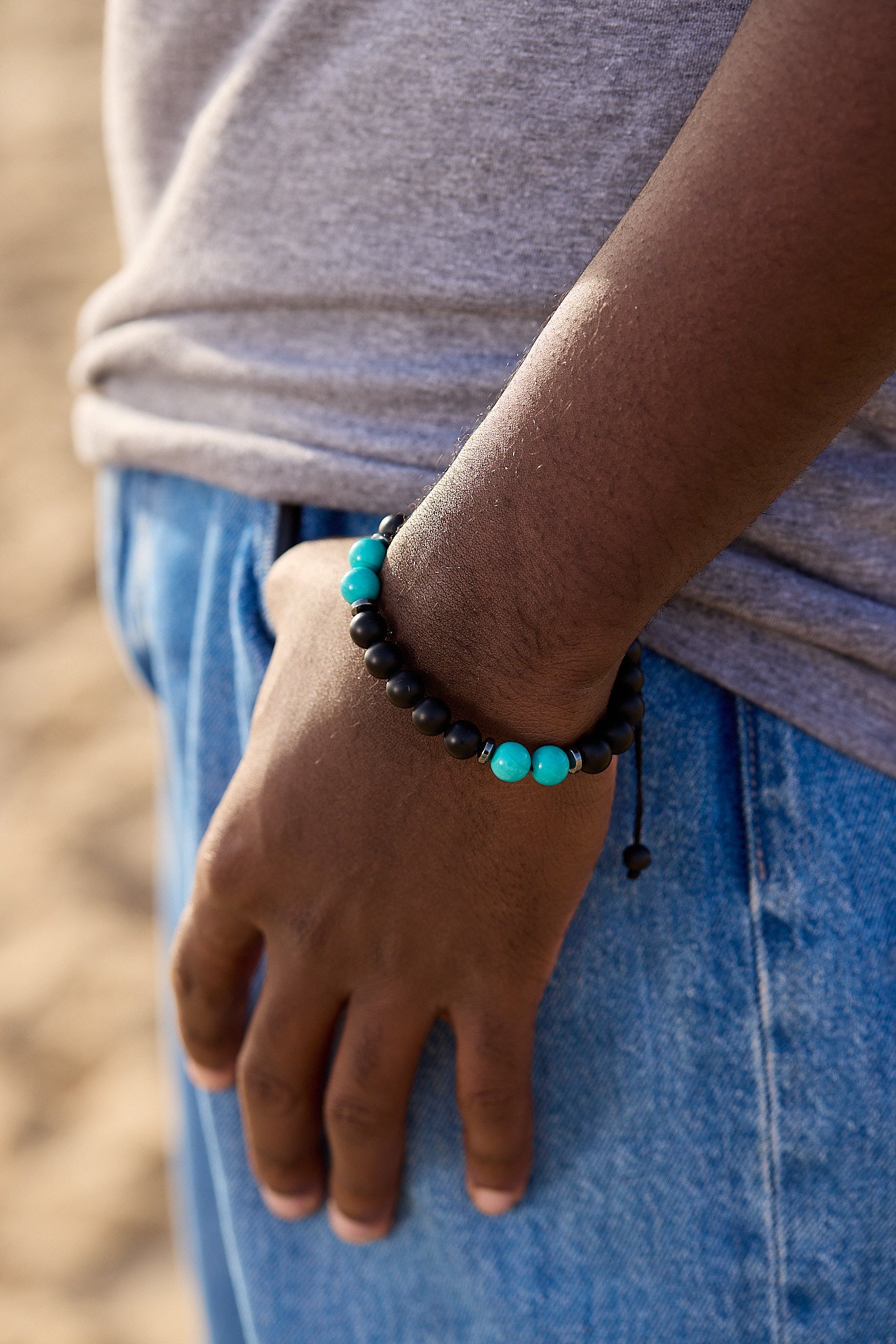 Hand wearing a black and turquoise beaded bracelet with blurred background