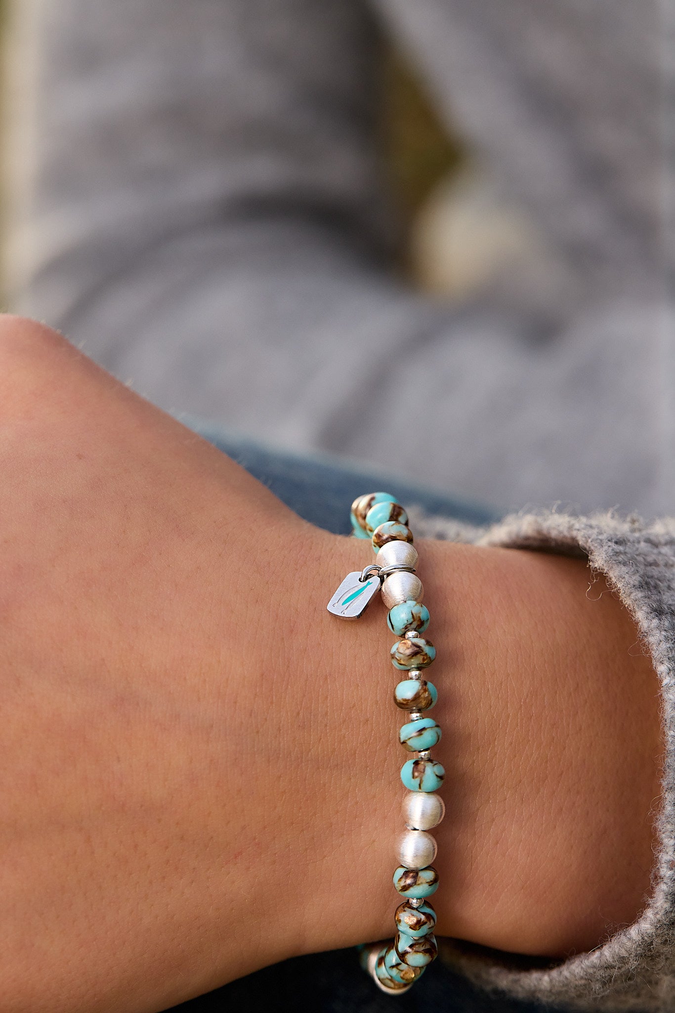 Close-up of a bracelet with turquoise and white beads on a wrist.